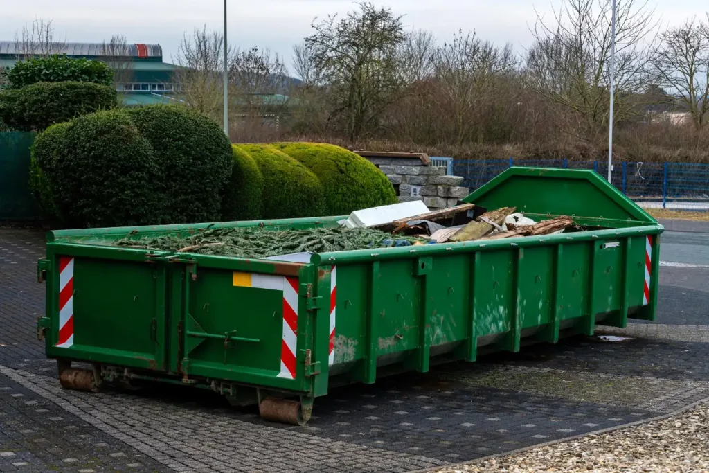 Grüner Bauschuttcontainer mit rot-weißen Warnstreifen gefüllt mit Baustellenabfällen und Holzresten, Container mieten Wien