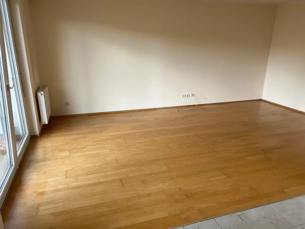 Räumung nach Zwangsversteigerung abgeschlossen: leeres Zimmer mit Parkettboden, Heizkörper und Balkontür