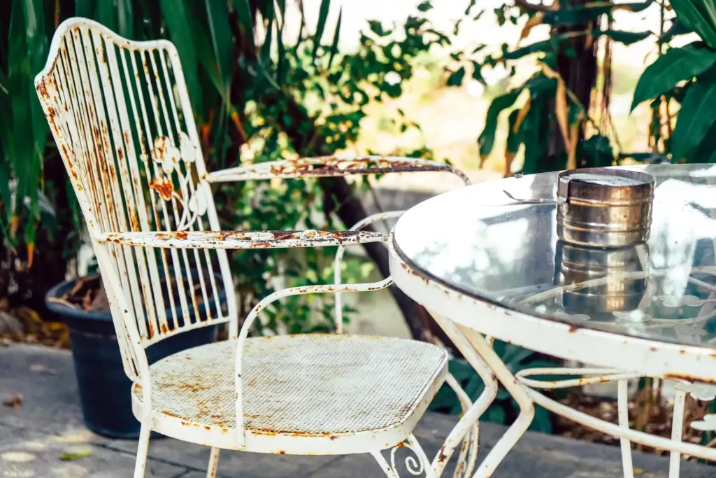 Rostige Sitzgruppe aus Metall mit Glastischplatte auf einer Terrasse, ein Fall für den Altmetallcontainer