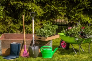 Werkzeug-Checkliste für die Schrebergarten Entrümpelung: Schaufel, Rechen, Schubkarre und Gummistiefel auf grünem Rasen